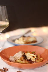 Plate with pork belly roast, mashed potatoes and roasted vegetables. Glass of white wine in the background. Served on a holiday table. Selective focus.