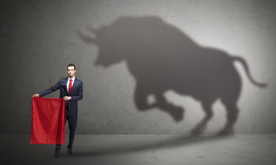 Businessman standing with red cloth in his hand and big bull shadow on the wall
