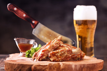 Roasted spare ribs on a wooden board with meat hatchet, BBQ sauce and glass of beer on a rustic wooden table