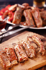 Roasted spare ribs on a wooden board with fork, knife and glass of beer on a rustic wooden table