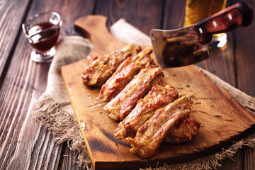 Roasted spare ribs on a wooden board with meat hatchet, BBQ sauce and glass of beer on a rustic wooden table