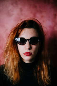close up portrait of a ginger woman with glasses in front of a red textured backgound