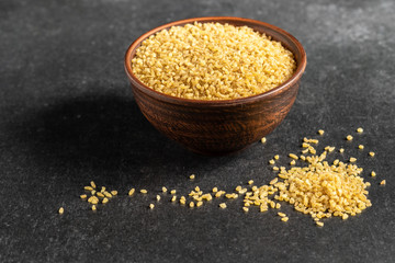 useful bulgur groats in ceramic dishes on a dark, gray, stone background
