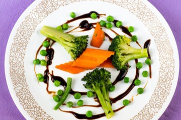 Carrot,broccoli and peas on white plate on violet background.