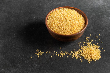useful bulgur groats in ceramic dishes on a dark, gray, stone background