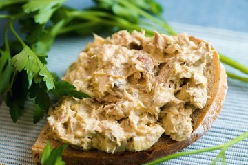 Sliced bread with fish spread, parsley leaf on blue.
