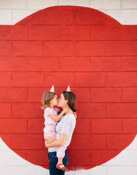 Mother kissing her daughter in front of wall
