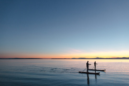 Couple stand up paddle boarding together at sunrise