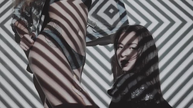 Two beautiful women in lingerie and jacket dancing with projected pattern on them. Music, nightclubs, shows and entertainment concept - video in slow motion