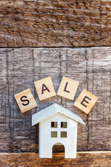 Miniature toy model house with inscription SALE letters word on wooden backdrop. Eco Village, abstract environmental background. Real estate mortgage property insurance sweet home ecology sale concept