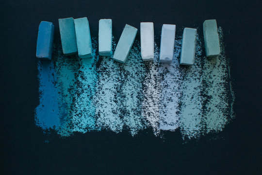 Assorted blue soft pastel chalks and it's swatches on black paper