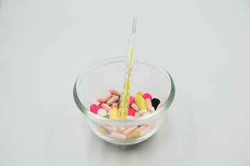 Assorted pharmaceutical medicine pills, tablets and capsules with thermometer on glass bowl