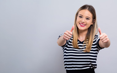 Young woman giving thumbs up on a gray background