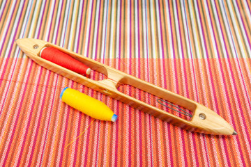 Wooden weaving shuttle with sewing thread on woven cotton.