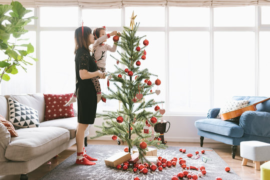 A cute  girl and her mother decorating christmas tree at home