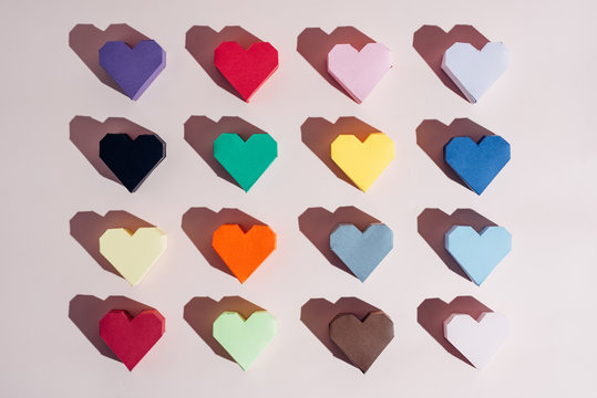 Various color hand crafted paper hearts from overhead on a pink background