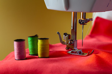 Spools of thread and a presser foot of sewing machine on a red cloth