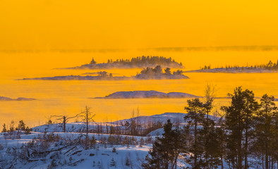 Sunset on the winter lake. Fog from heavy frost, soaring water at sunset. Lake in the winter at sunset in the bitter cold. Ladoga granite islands, skerries.
