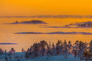 Sunset on the winter lake. Fog from heavy frost, soaring water at sunset. Lake in the winter at sunset in the bitter cold. Ladoga granite islands, skerries.