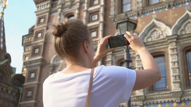 Woman taking pictures of Church of the Savior on Blood with smartphone.