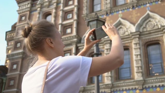 Woman taking pictures of Church of the Savior on Blood with smartphone.