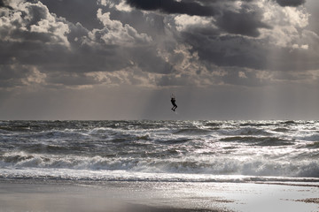 Fototapeta premium Silhouette of a jumping kitesurfer with sun coming through clouds
