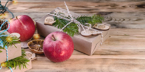 Fototapeta na wymiar Web banner Christmas background. Red apples, gifts, fir branches and cones on a wooden background