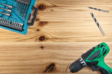 Green cordless screwdriver with bits and drills  in blue case on wooden background

