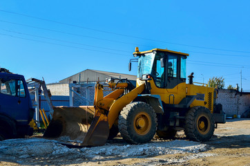 Fototapeta premium Yellow excavator on the construction site is preparing to load the soil into the dump truck. Wheel loader with iron bucket