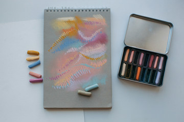 Metal box with assorted soft pastels and notebook with abstract drawing made with it