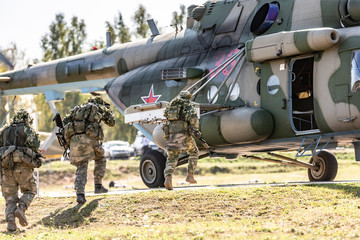 Military helicopter standing on the ground and soldiers loading into it.