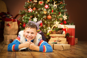 Christmas Child under Xmas Tree, Happy Boy Kid lying on wood floor front of New Year Presents Gifts