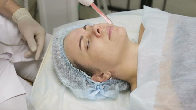 Woman getting facial electric darsonval therapy at cosmetology clinic