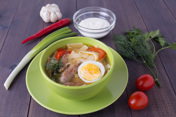 Chicken soup with noodles, egg and sour cream in a plate on a wooden background