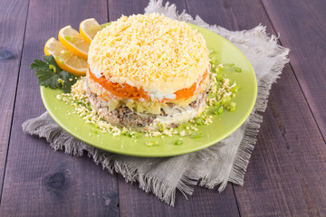 Mimosa fish salad layers in the shape of a circle with lemon slices on a wooden background