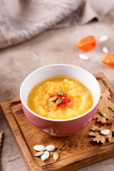 Pumpkin puree soup with pumpkin seeds on a decorative board decorated with autumn leaves.