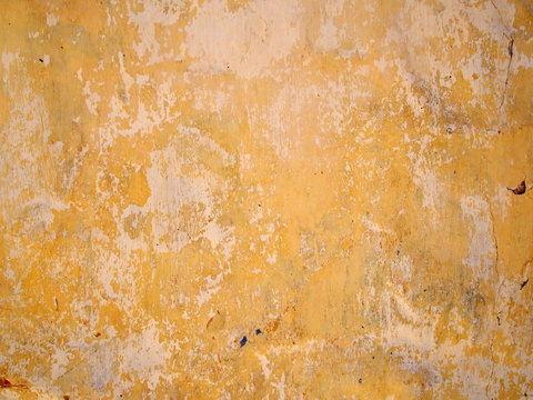 peeling layers of yellow and beige paint on a cement wall with cracks and random splashes of other colors
