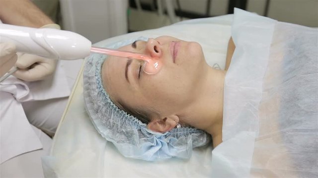 Woman getting facial electric darsonval therapy at cosmetology clinic