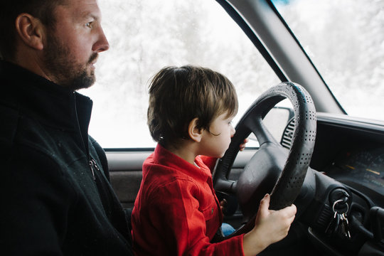 son sits on dad's lap helping drive while in open mountain area