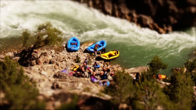 Tilt shift: Miniature man pumping up a raft at the river prior to start of White river rafting tour -wide shot
