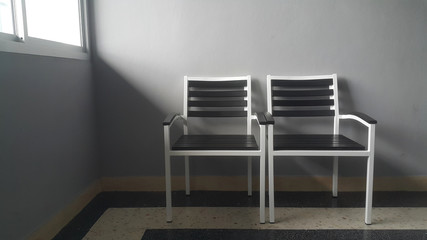 Two modern style chairs are placed in front of plain gray walls. And the light from the windows inside a building.