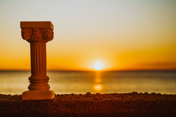 Greek column on shore and sunset over sea surface