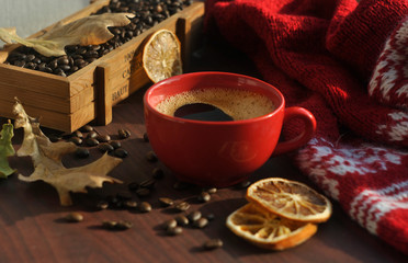 Fototapeta na wymiar A red cup of coffee, a box of coffee, coffee beans, a warm knitted scarf and dry leaves are on the wooden table.