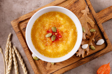 Pumpkin soup puree in a ceramic bowl with pumpkin seeds and spicy chili pepper seasoning.