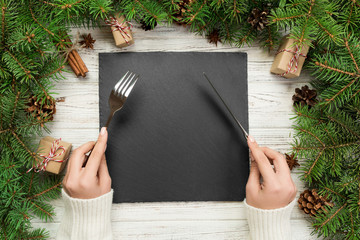 top view girl holds fork and knife in hand and is ready to eat. Empty black slate square plate on...