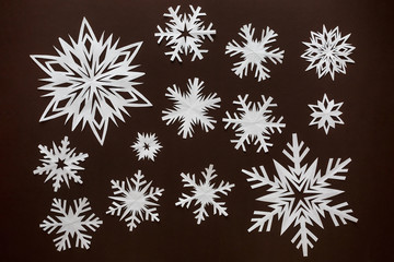 White paper snowflakes different shapes and sizes on brown cardboard background. Top view.