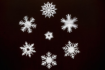 White paper snowflakes different shapes and sizes on brown cardboard background. Top view.