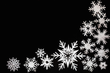 White paper snowflakes different shapes and sizes on black cardboard background. Top view.