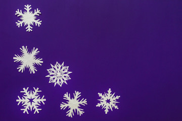 White paper snowflakes different shapes and sizes on violet background. Top view.