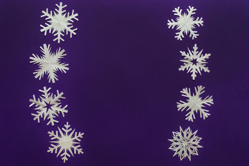 Fototapeta na wymiar White paper snowflakes different shapes and sizes on violet background. Top view.